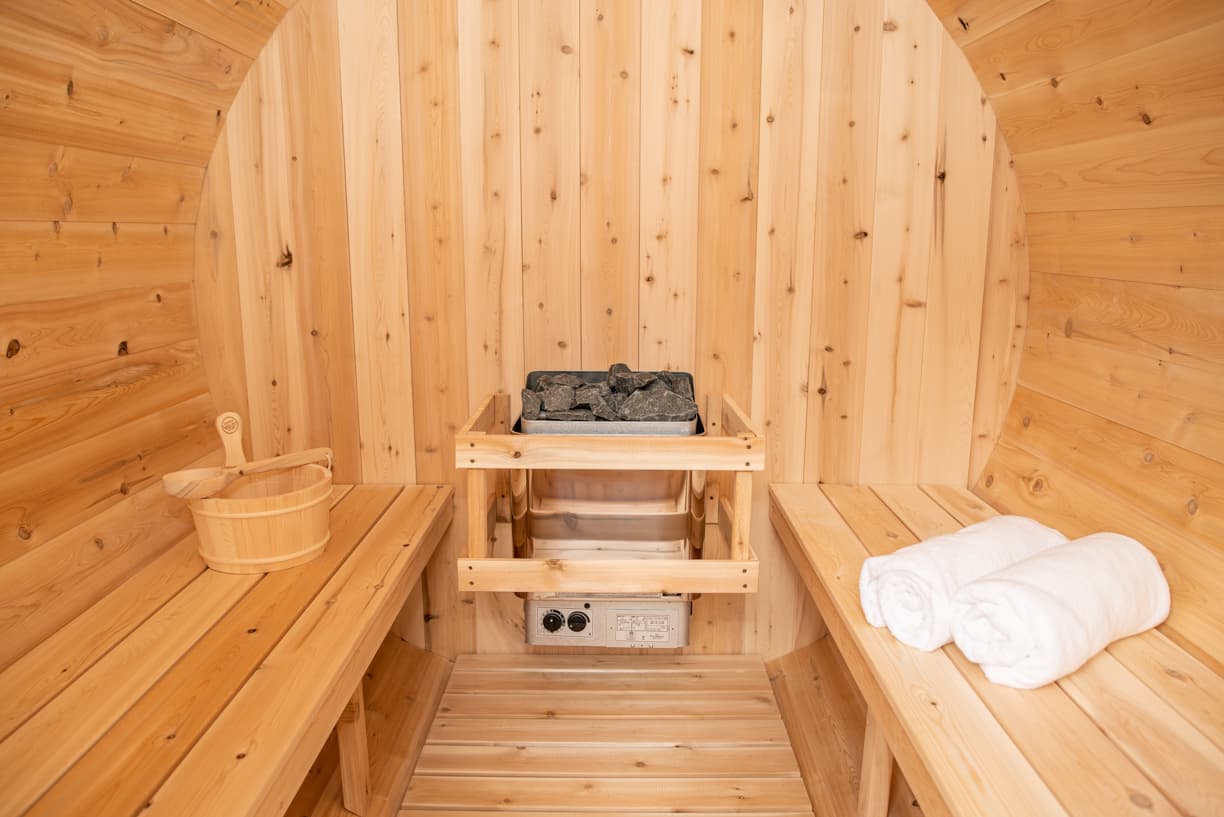 Canadian Timber barrel sauna by Dundalk, features natural wood interior, stone heater, two wooden benches, and towel storage