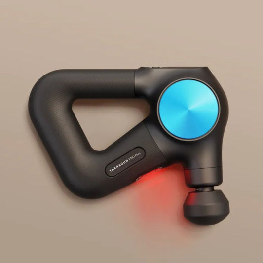 Black handheld Theragun pro Plus massager with blue and red lights on a beige background