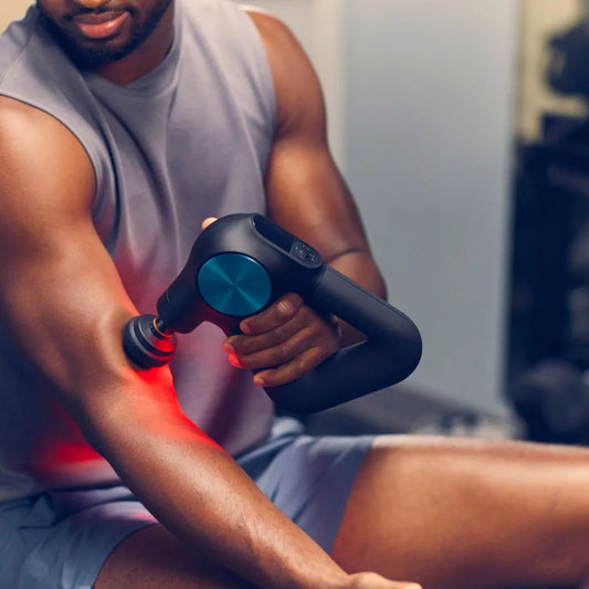 Man using a massage gun on his arm in a gym setting